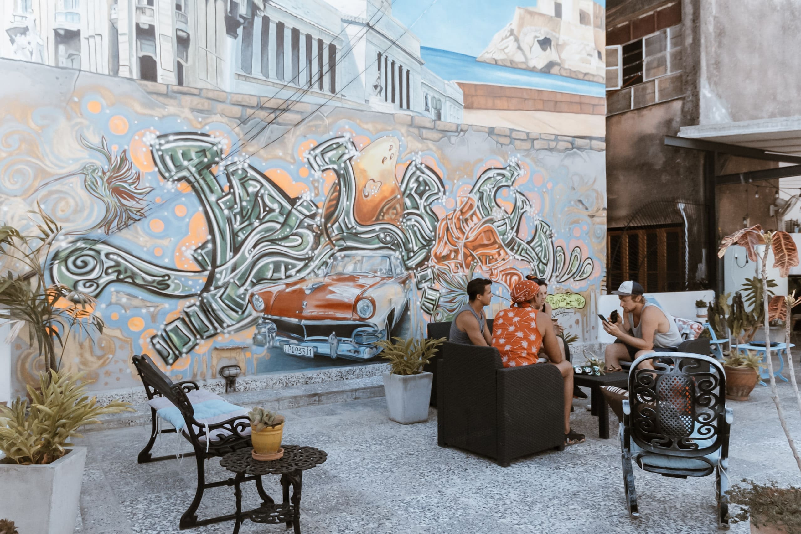 Menschen sitzen vor einem Graffiti auf einer Dachterrasse in Kuba